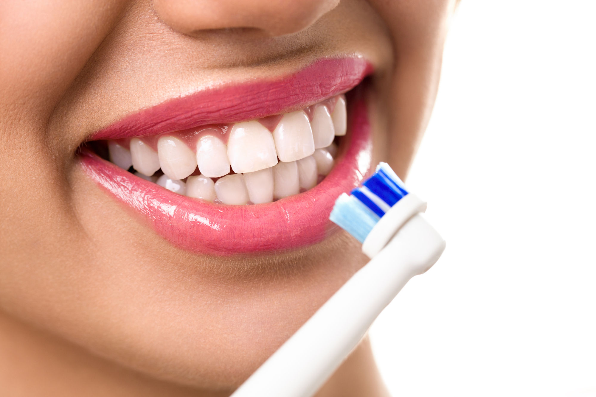 woman with bright, perfect teeth brushing with an electric toothbrush