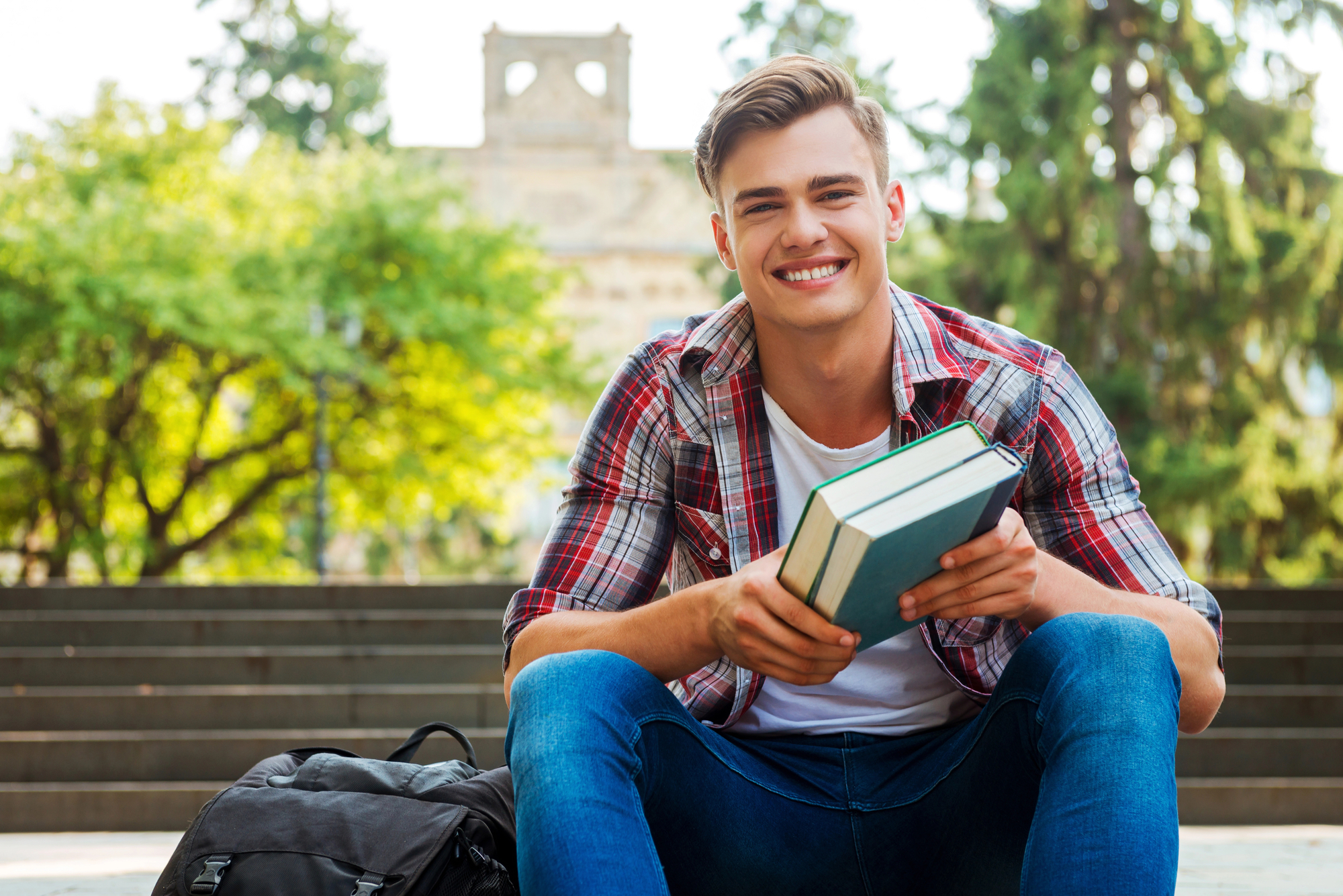 male college student holding text books while sitting on bench