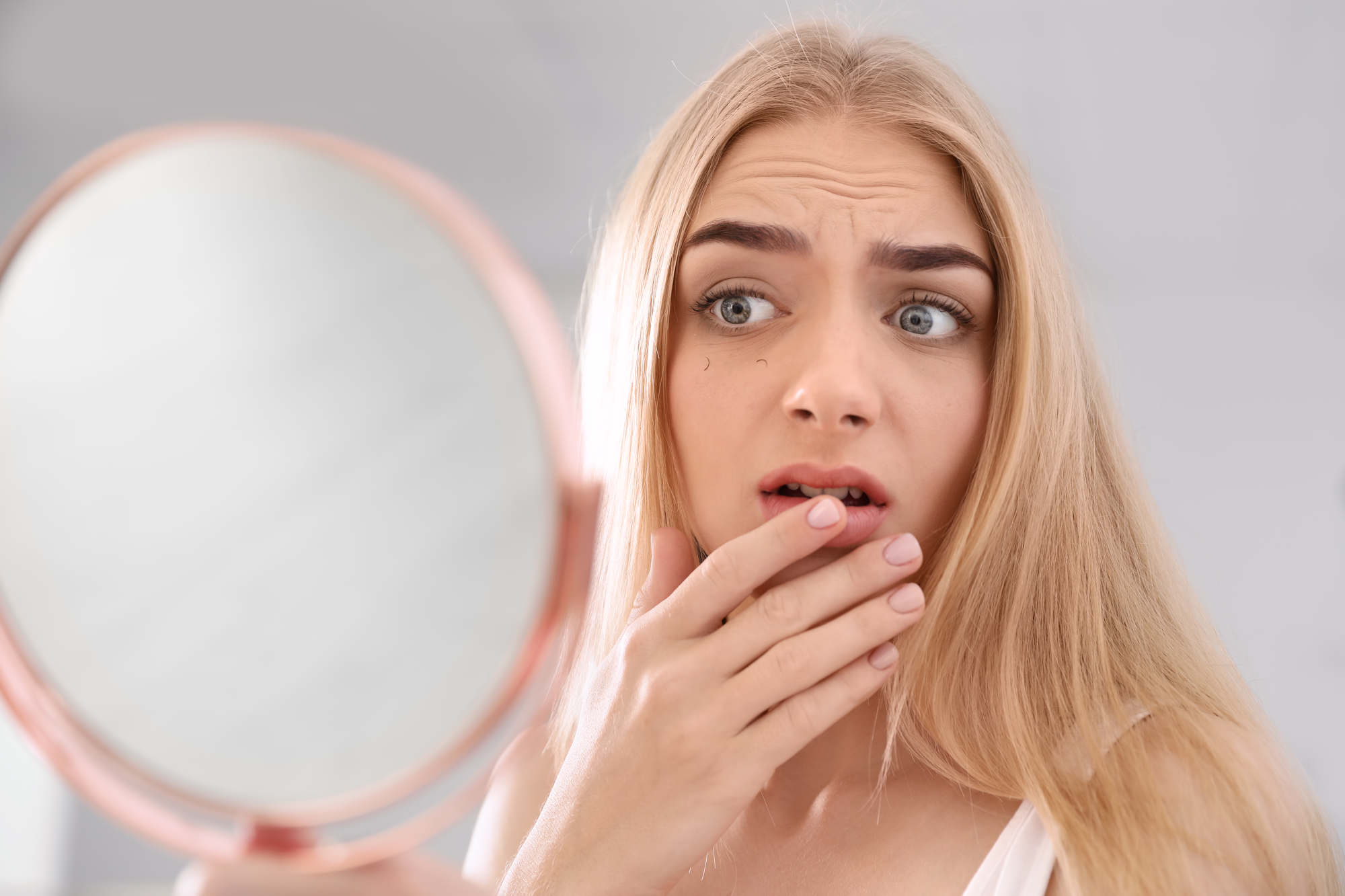 woman looking at her crooked teeth in the mirror