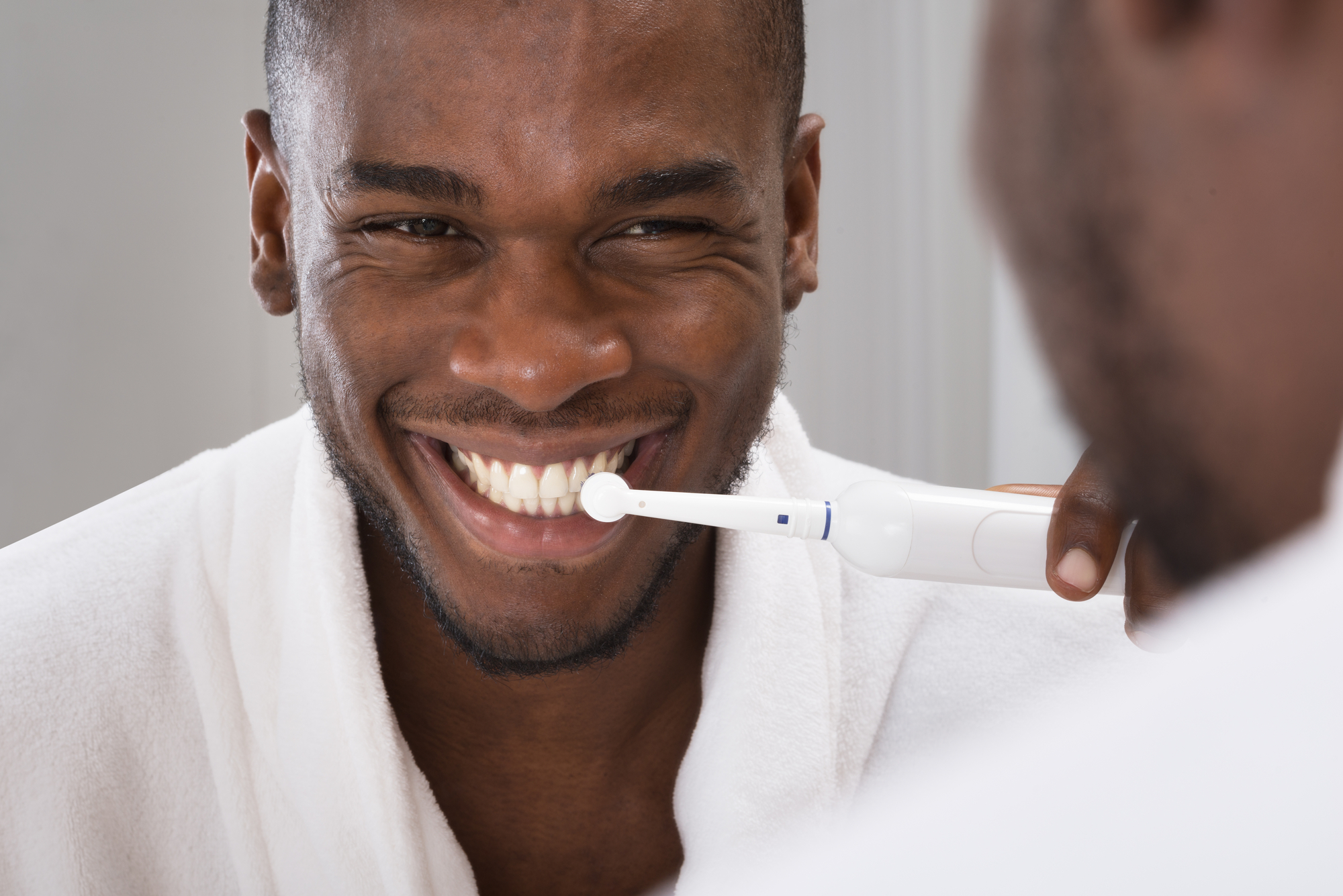 black man using electric toothbrush in mirror
